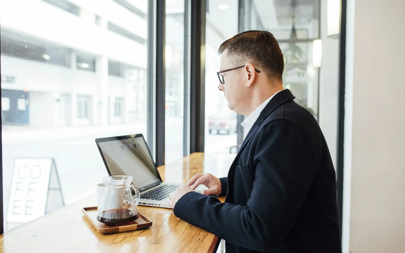 A professional working at a laptop beside a bright office window.