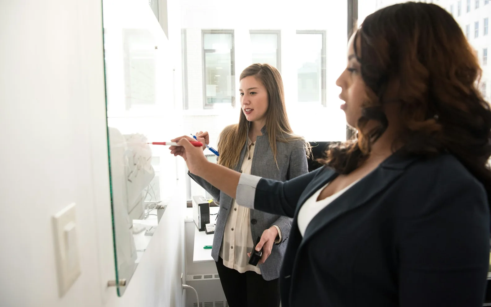 Two colleagues developing ideas together on a glass board.